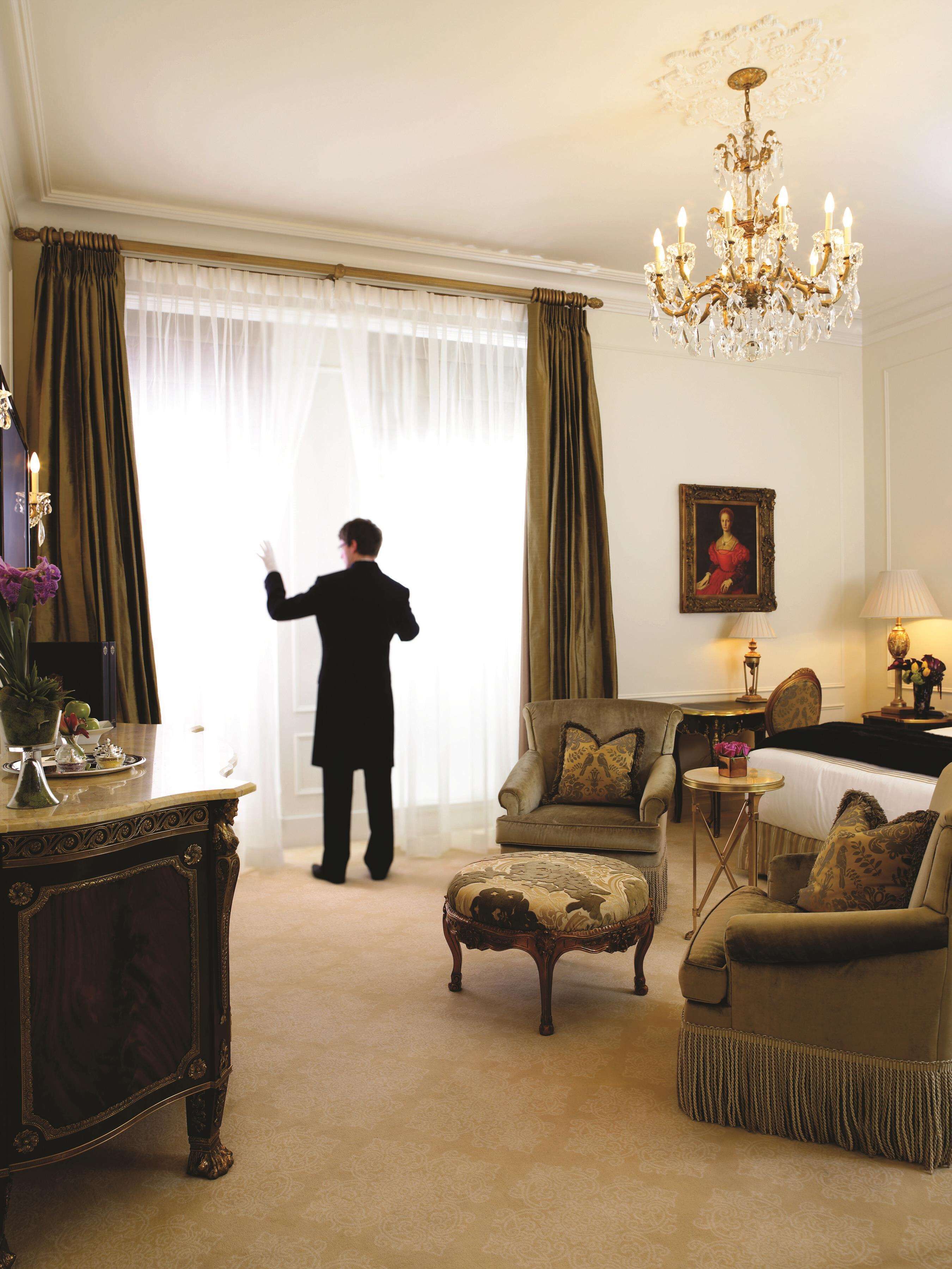Quarto com uma grande janela, um candelabro, um quadro e uma mesa com abajur.