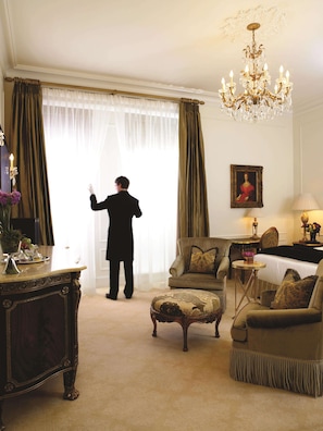 A room with a large window, a chandelier, a painting, and a table with a lamp.