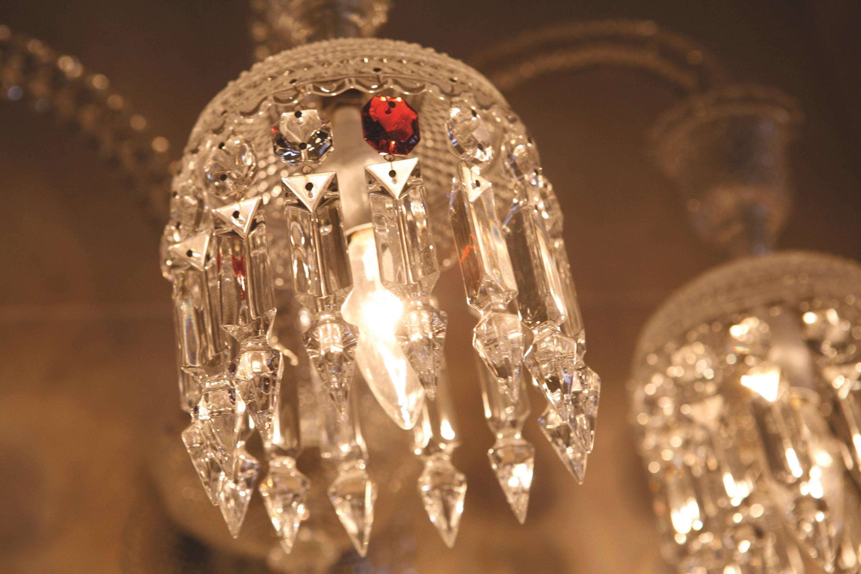 A close-up of a crystal chandelier with multiple hanging crystals and a central red gem.