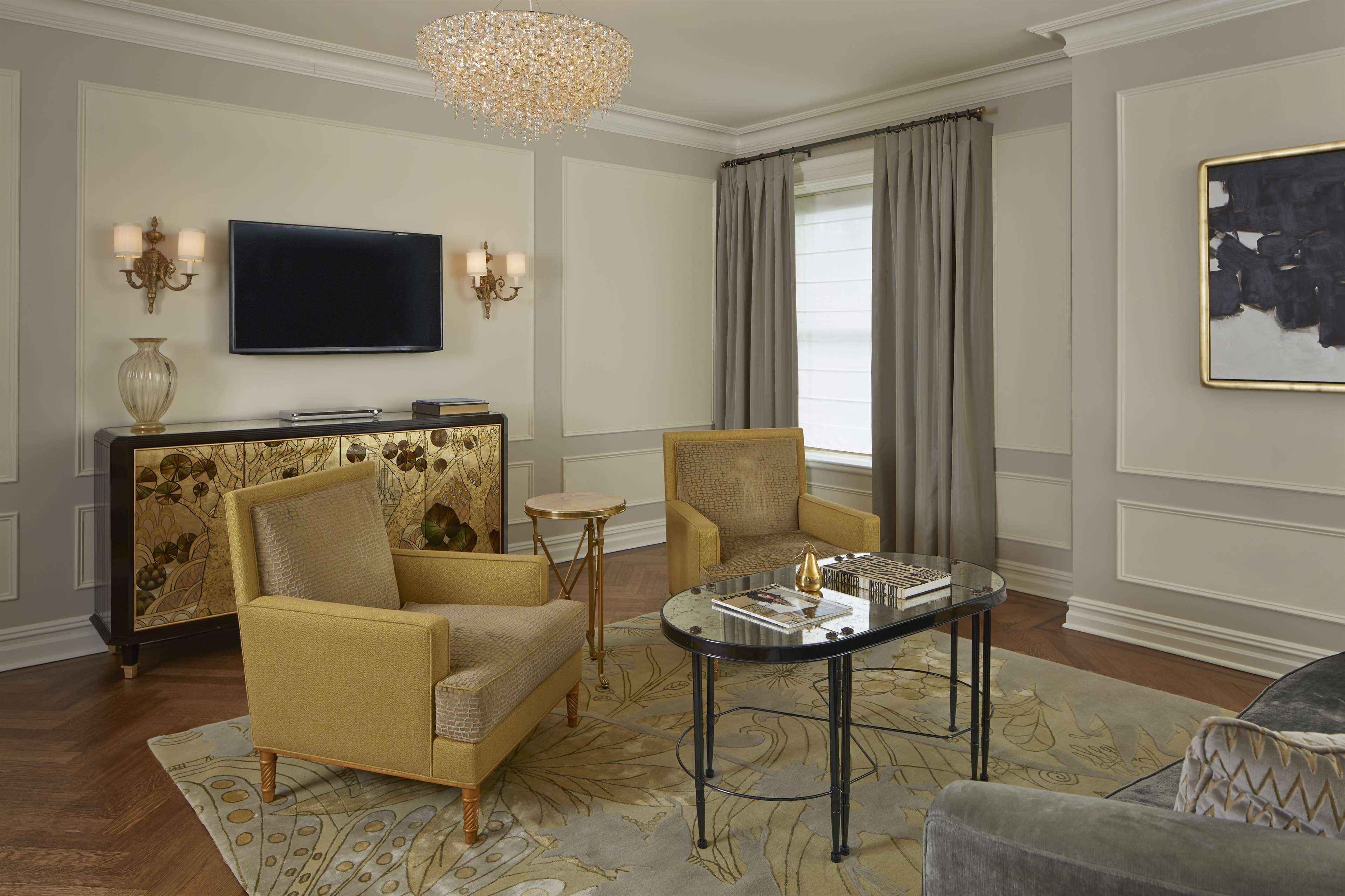 A living room with a sofa, two armchairs, a coffee table, a TV, and a chandelier.
