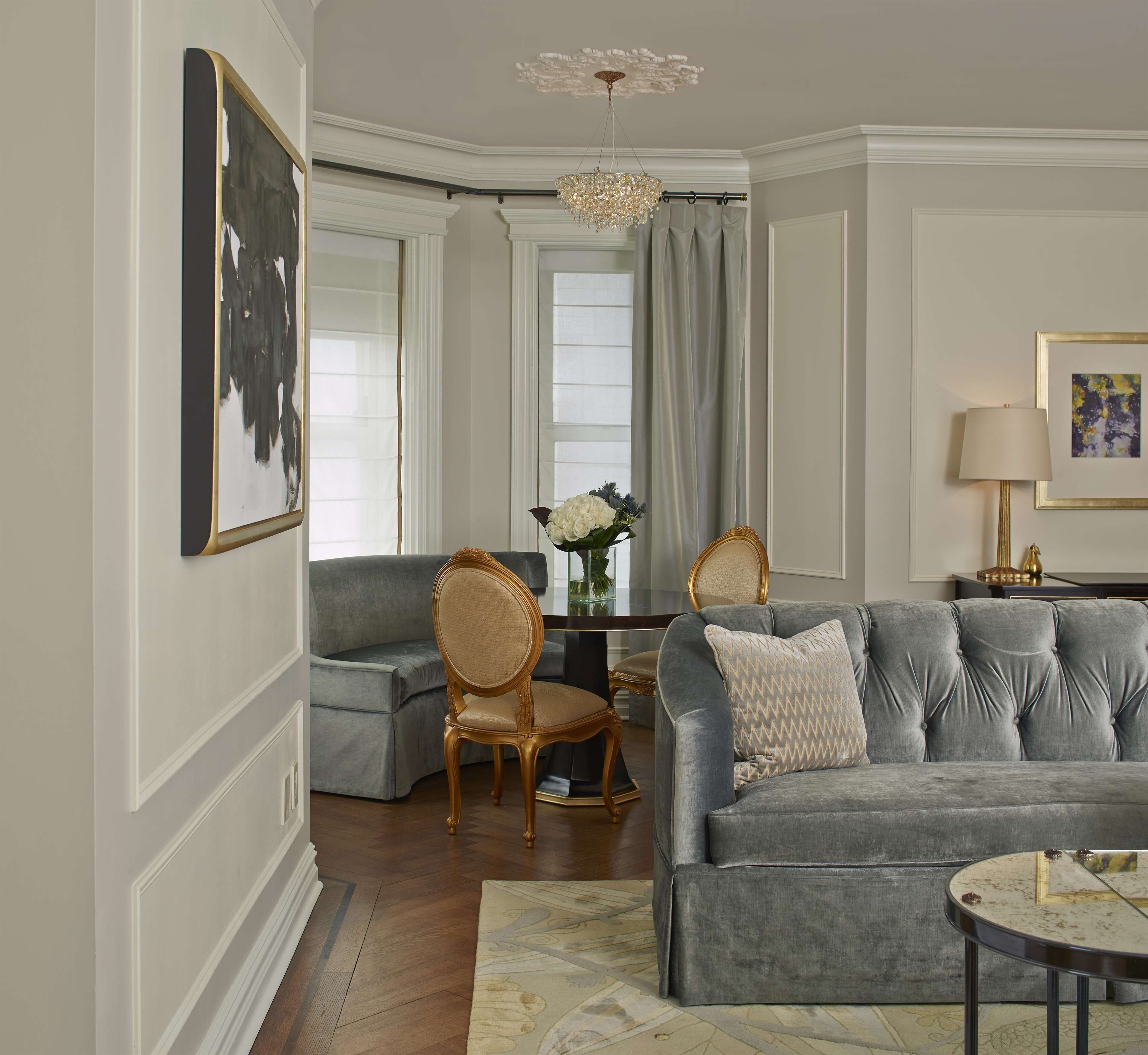 A living room with a grey sofa, a matching armchair, a small table with a vase of flowers, and a chandelier.