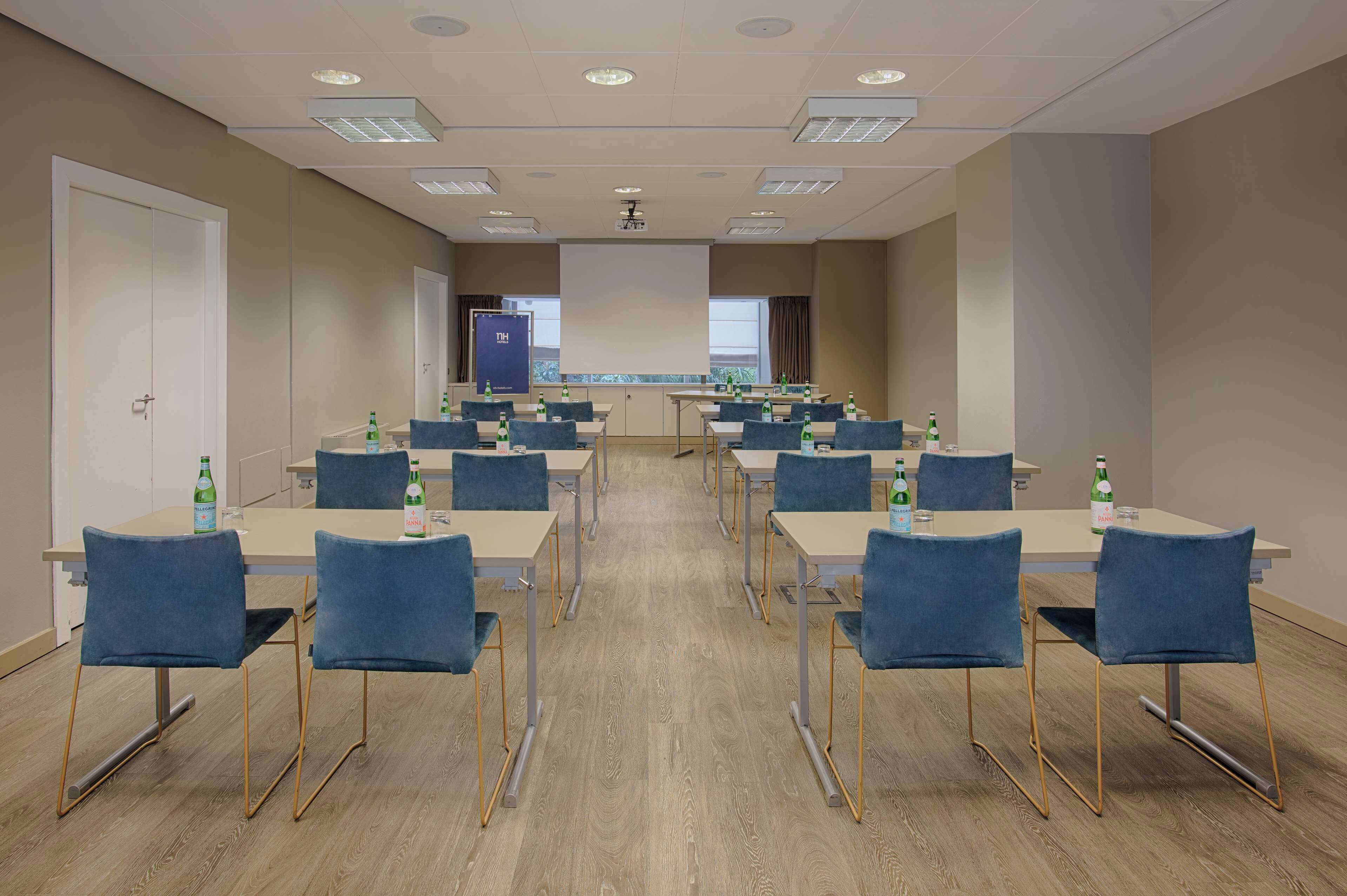 Una sala de conferències amb diverses taules i cadires, equipada amb projectors i pantalles, i amples d'aigua sobre les taules.