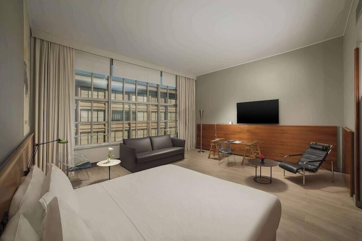 Habitació d'hotel amb un llit gran, un sofà, una televisió, una taula de treball i una cadira.