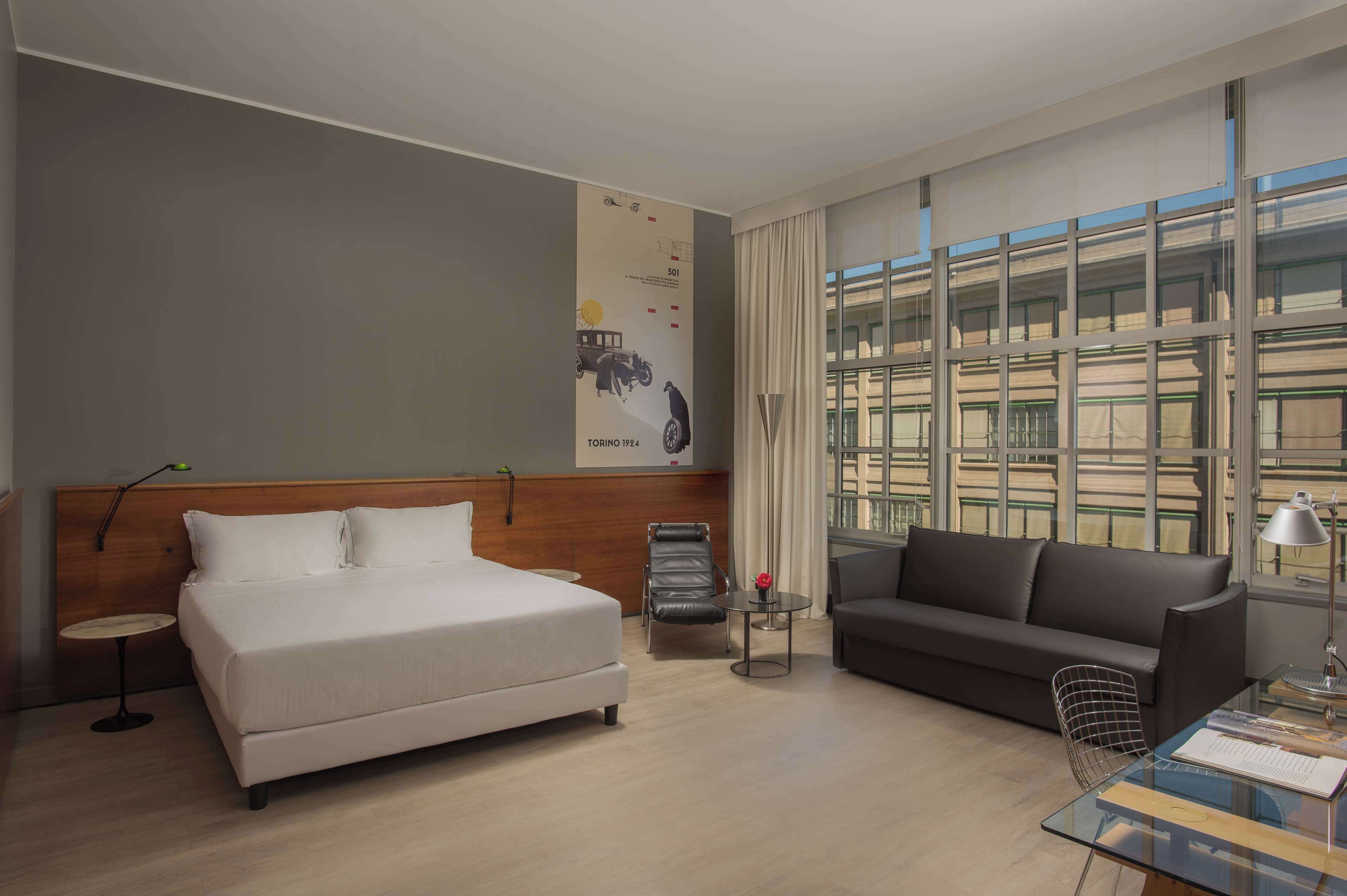 A modern hotel room with a large bed, a sofa, a small table, and a chair.