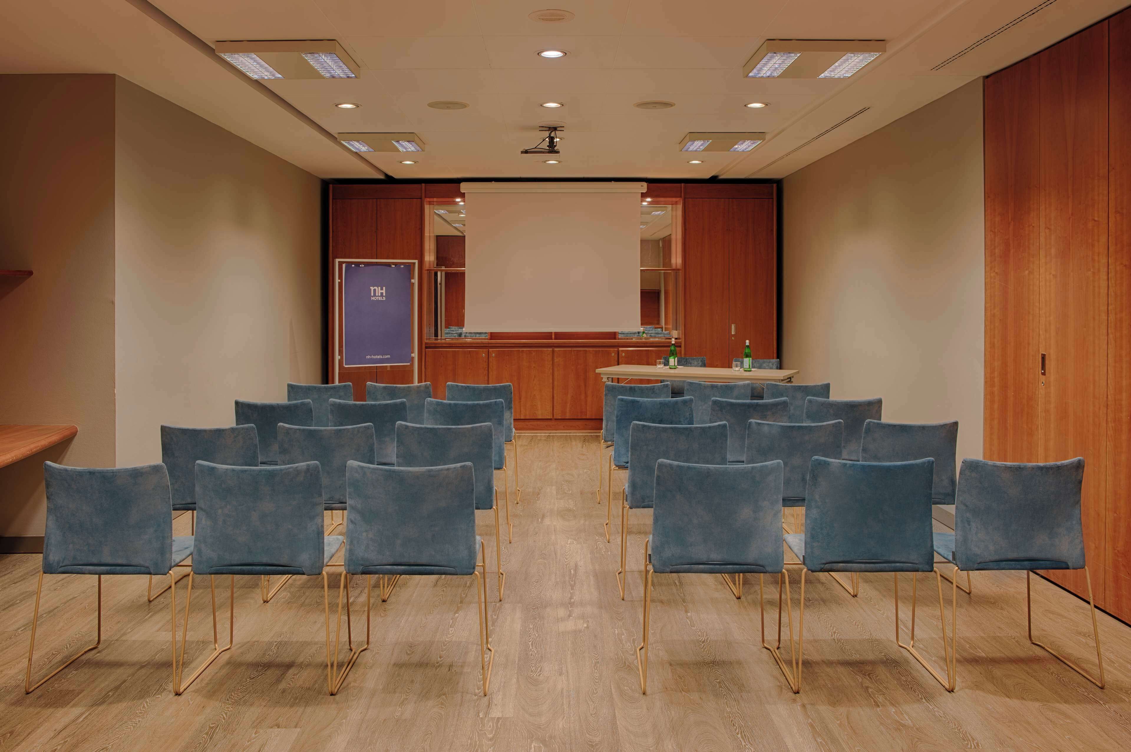 Ein Konferenzraum mit Reihen blauer Stühle, einem Rednerpult und einer Projektionsleinwand.