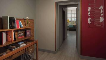 A hallway with a wooden bookshelf, a red bulletin board, and a window leading to another room.