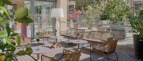 Una terraza en la azotea con mobiliario de mimbre, barandillas de vidrio y plantas en macetas.
