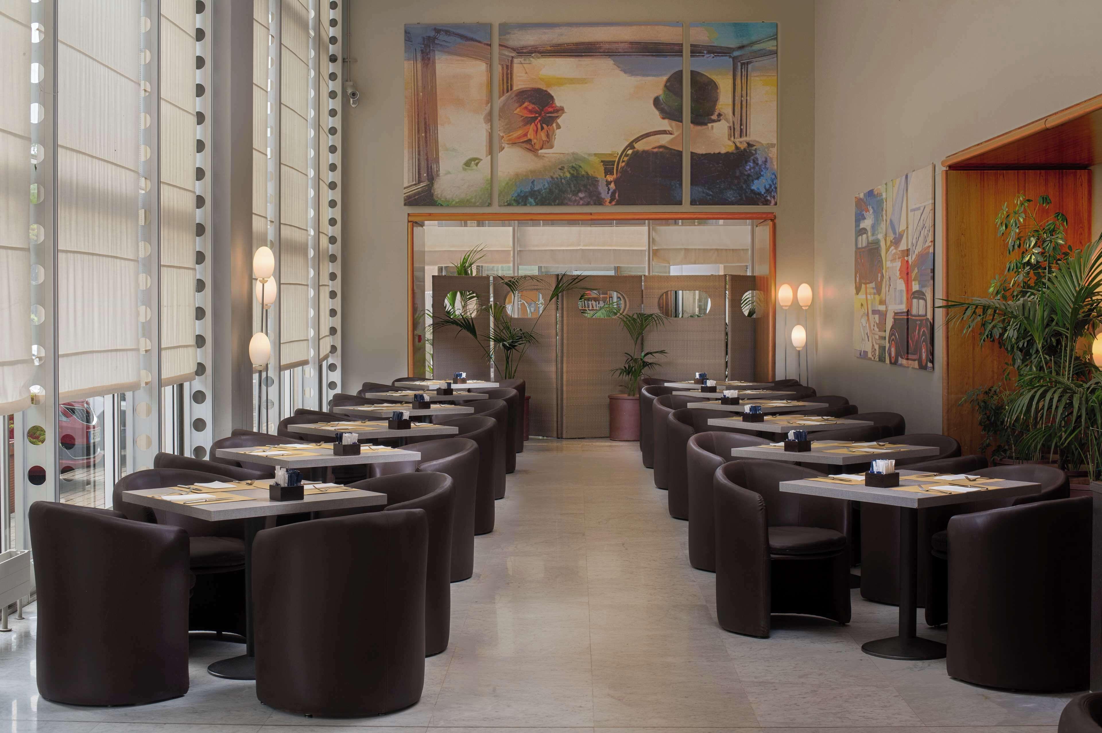 Un restaurante moderno con varias mesas y sillas, ventanas amplias y obras de arte en las paredes.