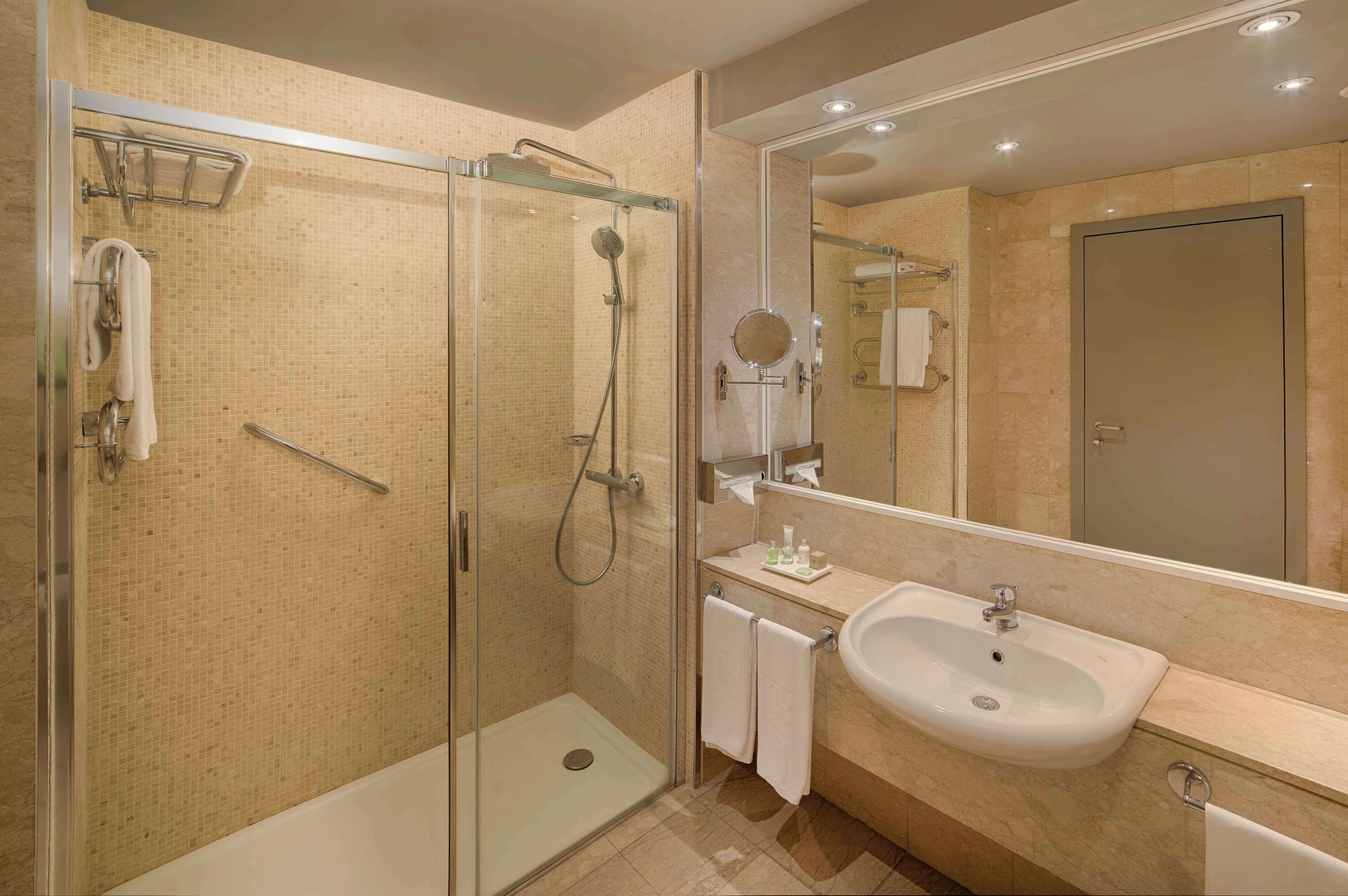 A modern bathroom with a glass-enclosed shower, a sink, and a large mirror.