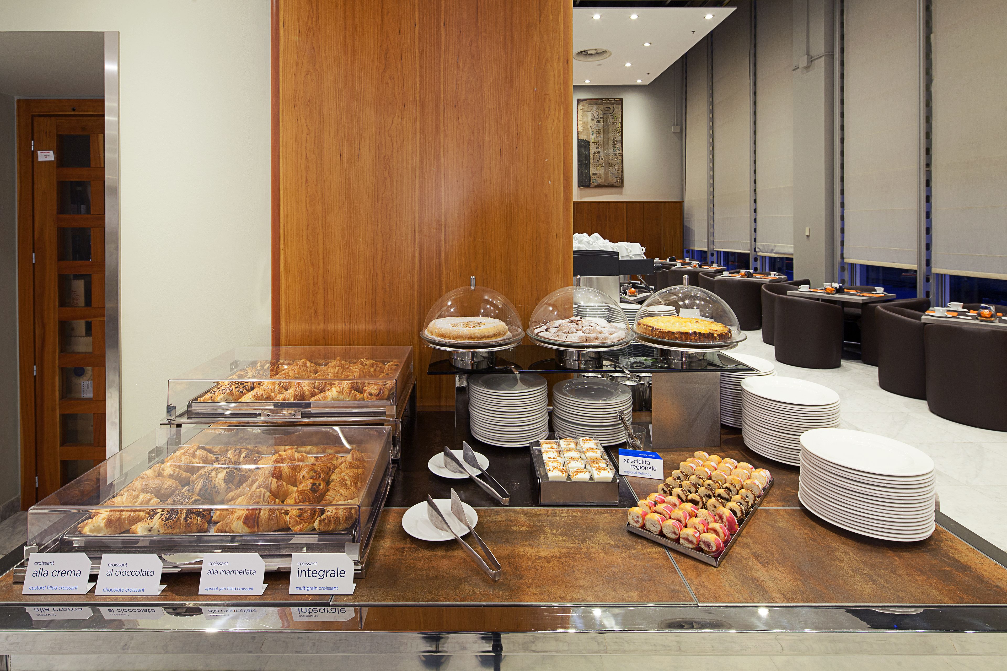 A buffet with various desserts and pastries, including croissants and cakes, displayed in clear containers.
