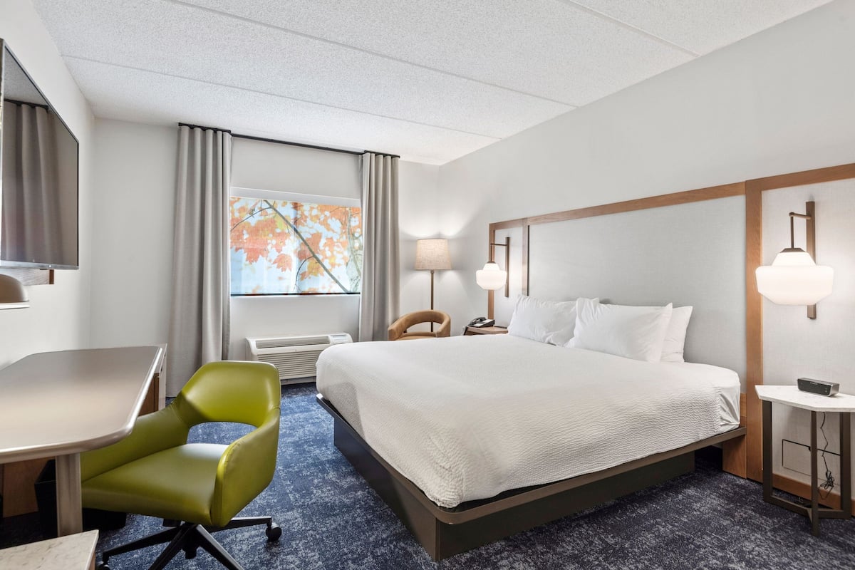A hotel room with a bed, desk, chair, and a window with curtains.