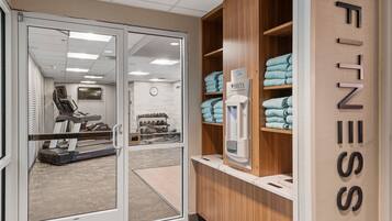 A fitness center with a treadmill, a wall clock, and neatly folded towels on shelves.