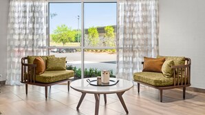Une pièce moderne avec deux fauteuils en bois, une table ronde et une grande fenêtre avec des rideaux.