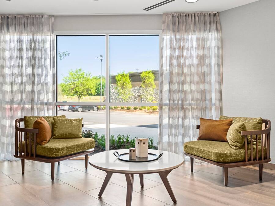 A modern room with two wooden armchairs, a round table, and a large window with curtains.