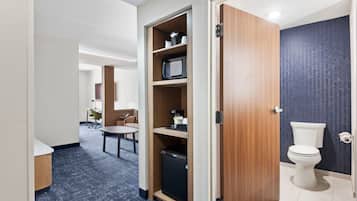 A compact hotel room with a kitchenette, a small dining area, and a bathroom with a toilet and sink.