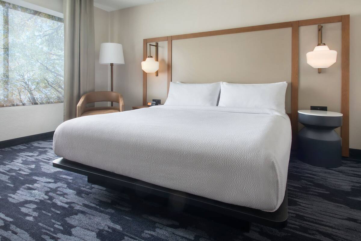 A neatly made bed with a headboard, a bedside lamp, and a nightstand with a lamp.