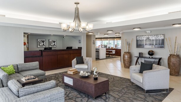 A modern hotel lobby with grey upholstered sofas, a dark brown coffee table, and a chandelier. - Wingate by Wyndham Shreveport Airport (Shreveport)