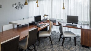 A modern hotel room with a wooden desk, two monitors, a keyboard, and a lamp. There are four chairs and a large window with curtains. - Wingate by Wyndham Shreveport Airport (Shreveport)