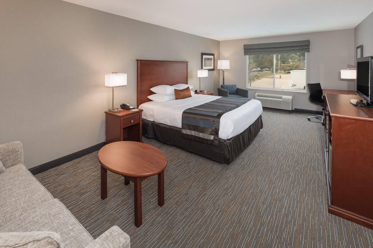 A hotel room with a bed, a desk, a chair, a TV, and a window.