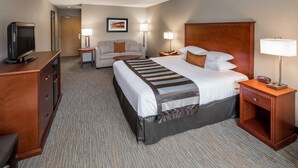 A hotel room with a bed, a desk with a television, a sofa, two bedside tables with lamps, and a framed picture on the wall. - Wingate by Wyndham Shreveport Airport (Shreveport)