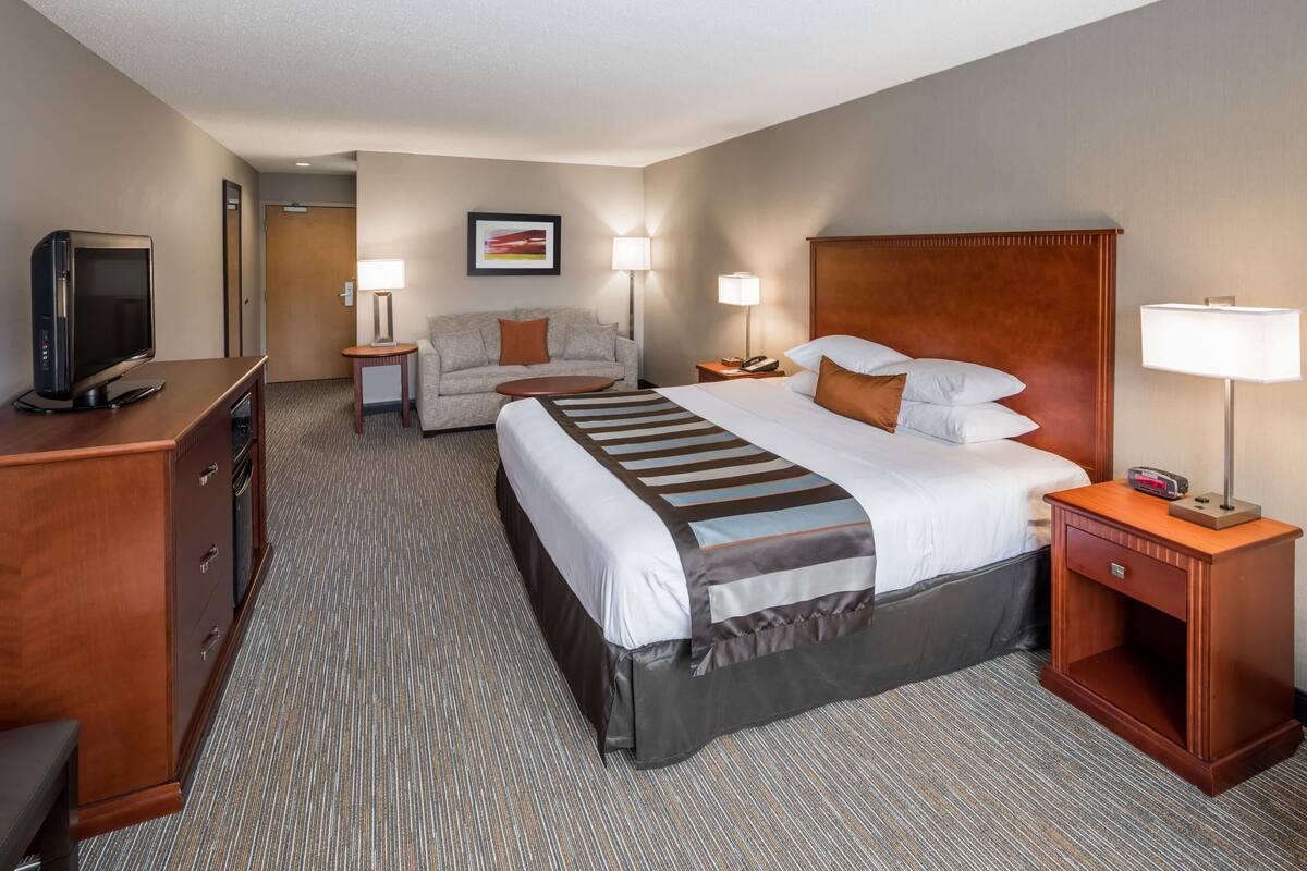A hotel room with a bed, a desk with a television, a sofa, two bedside tables with lamps, and a framed picture on the wall.