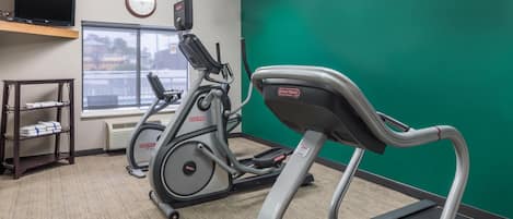 Un gimnasio con cintas de correr, una bicicleta estática y un televisor montado en la pared.