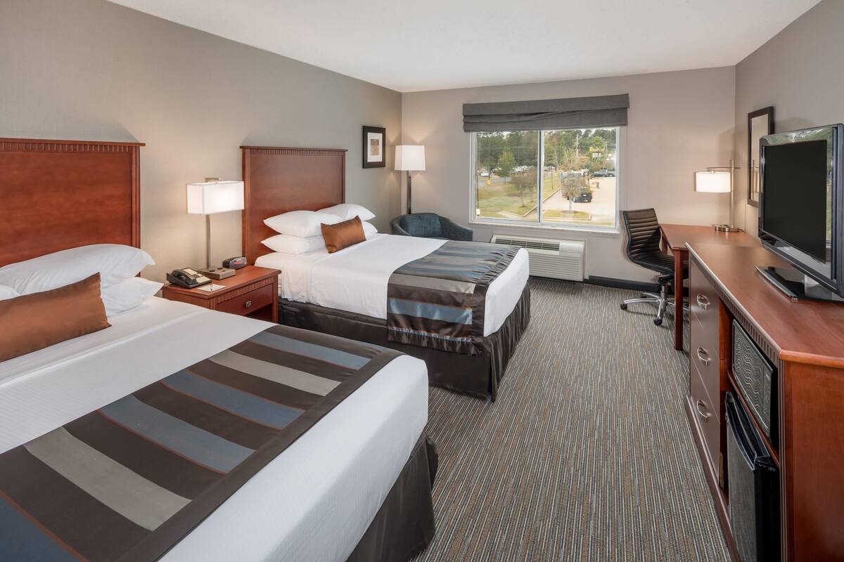 A hotel room with two beds, a desk, a TV, and a window with a view.