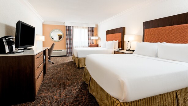 Ein Hotelzimmer mit einem großen Bett, einem kleineren Bett, einem Schreibtisch mit Fernseher und einem Spiegel.