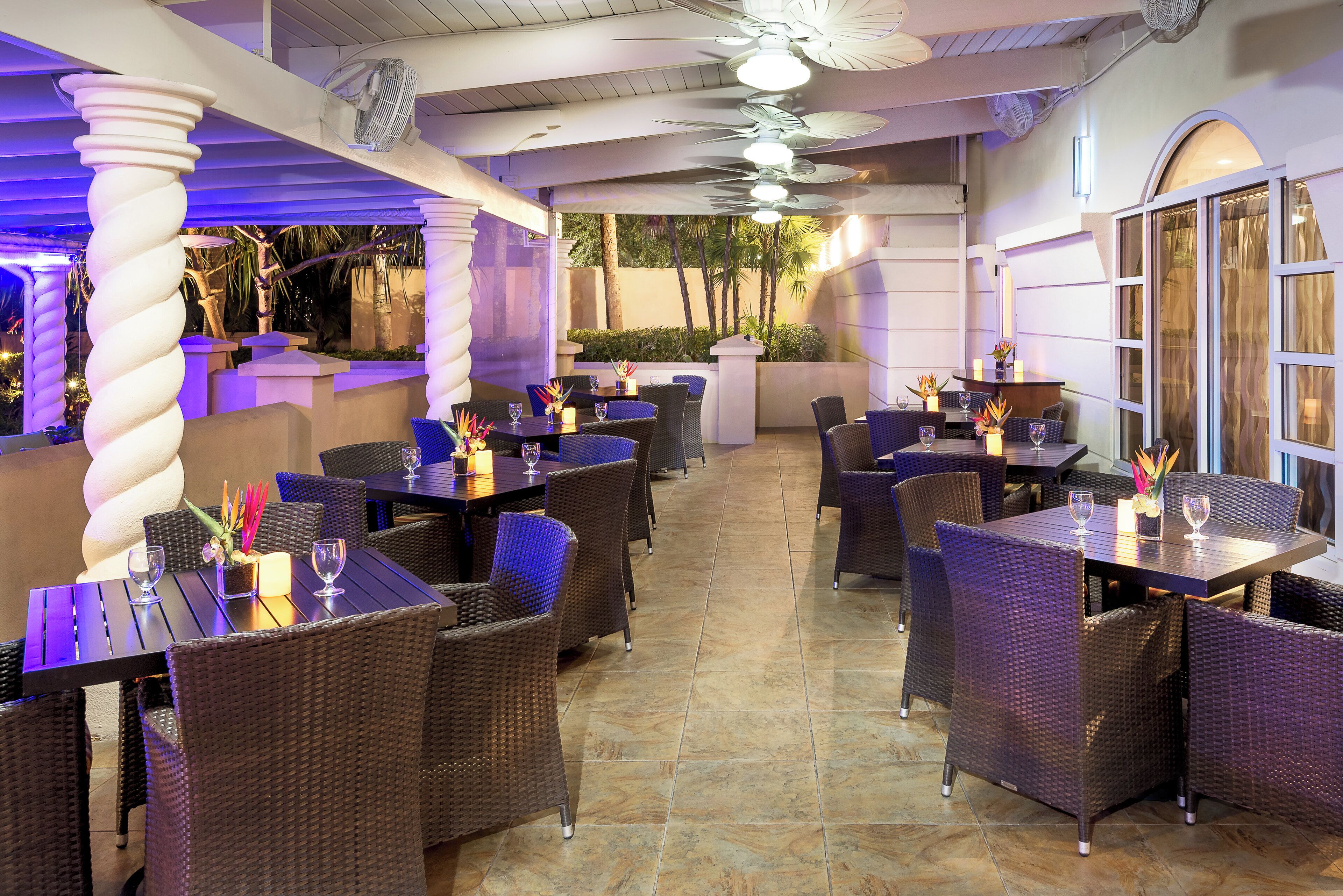 An outdoor dining area with wicker furniture and tables, some with candles and flowers.