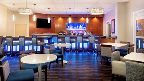 A bar area with multiple seating options, a television screen, and a variety of bottles on the shelves. - Holiday Inn Fort Lauderdale Airport by IHG (Hollywood)