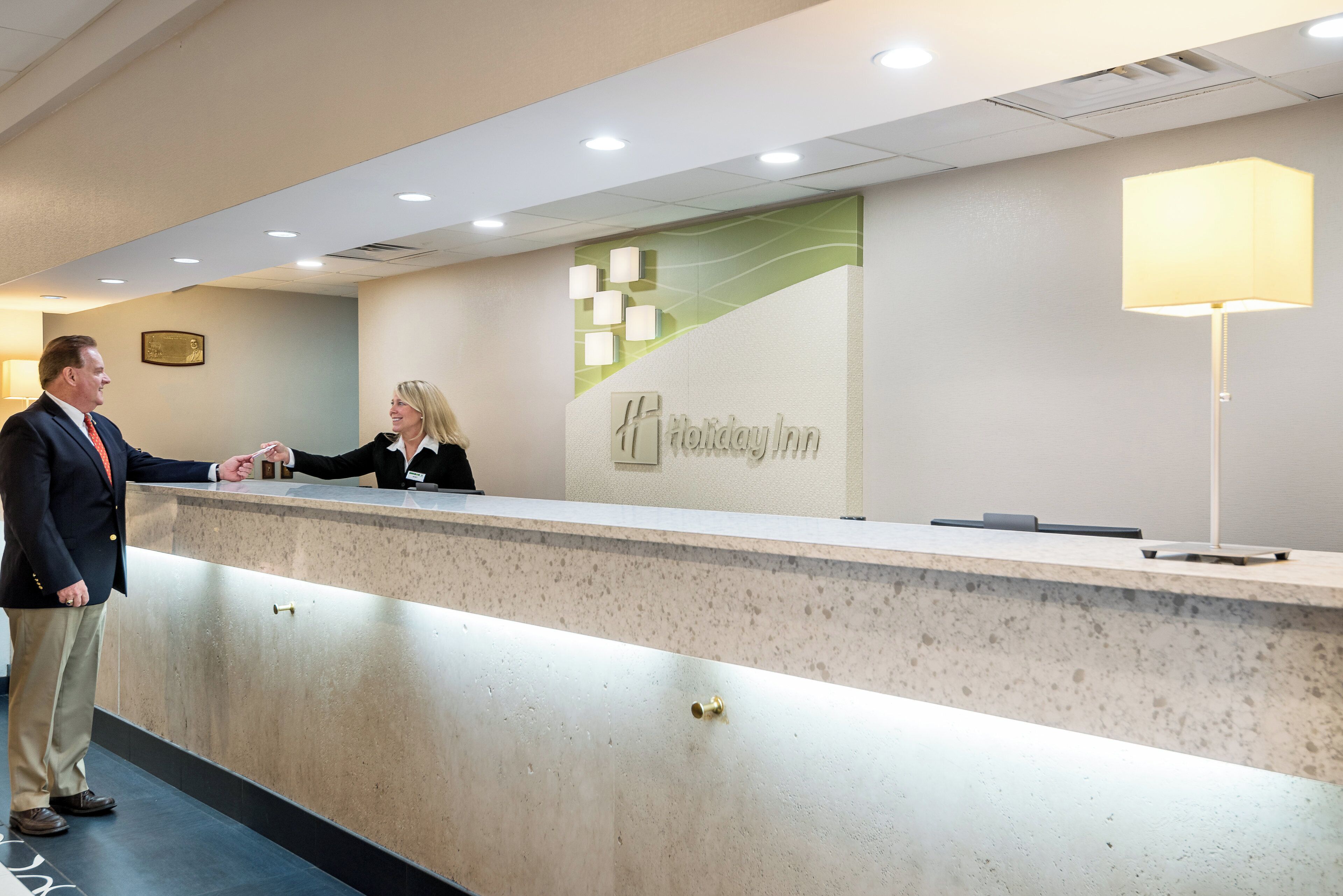 Un mostrador de recepción de hotel con una placa identificativa, una lámpara de pared y un mostrador.