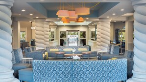 A modern lounge area with a curved seating arrangement, a water feature, and a view of the outdoors. - Holiday Inn Fort Lauderdale Airport by IHG (Hollywood)
