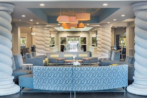 A modern lounge area with a curved seating arrangement, a water feature, and a view of the outdoors. - Holiday Inn Fort Lauderdale Airport by IHG (Hollywood)