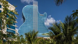Ein Gebäude mit einer gitarrenförmigen Fassade, umgeben von Palmen und anderer Bepflanzung.