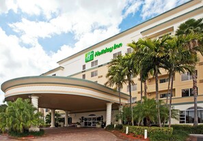 A Holiday Inn hotel with a curved entrance, palm trees, and a clear sky. - Holiday Inn Fort Lauderdale Airport by IHG (Hollywood)