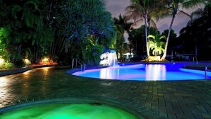 A nighttime swimming pool with a fountain, surrounded by palm trees and illuminated by artificial lighting. - Holiday Inn Fort Lauderdale Airport by IHG (Hollywood)
