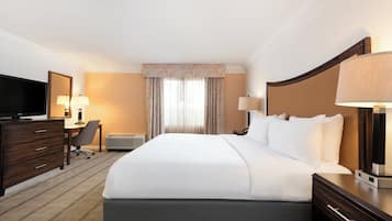 Een hotelkamer met een groot bed, een bureau met een televisie, een stoel, een bureaulamp en een nachtkastje met een lamp.
