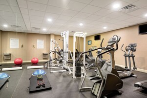 Un gimnasio con diversos equipos de ejercicio, incluyendo cintas de correr, una máquina de pesas y pelotas de ejercicio.