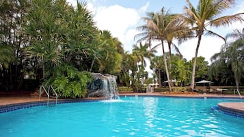 Una piscina con cascada, rodeada de palmeras y abundante vegetación.