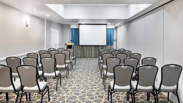 Un salón de conferencias con filas de sillas, un atril y una pantalla grande.