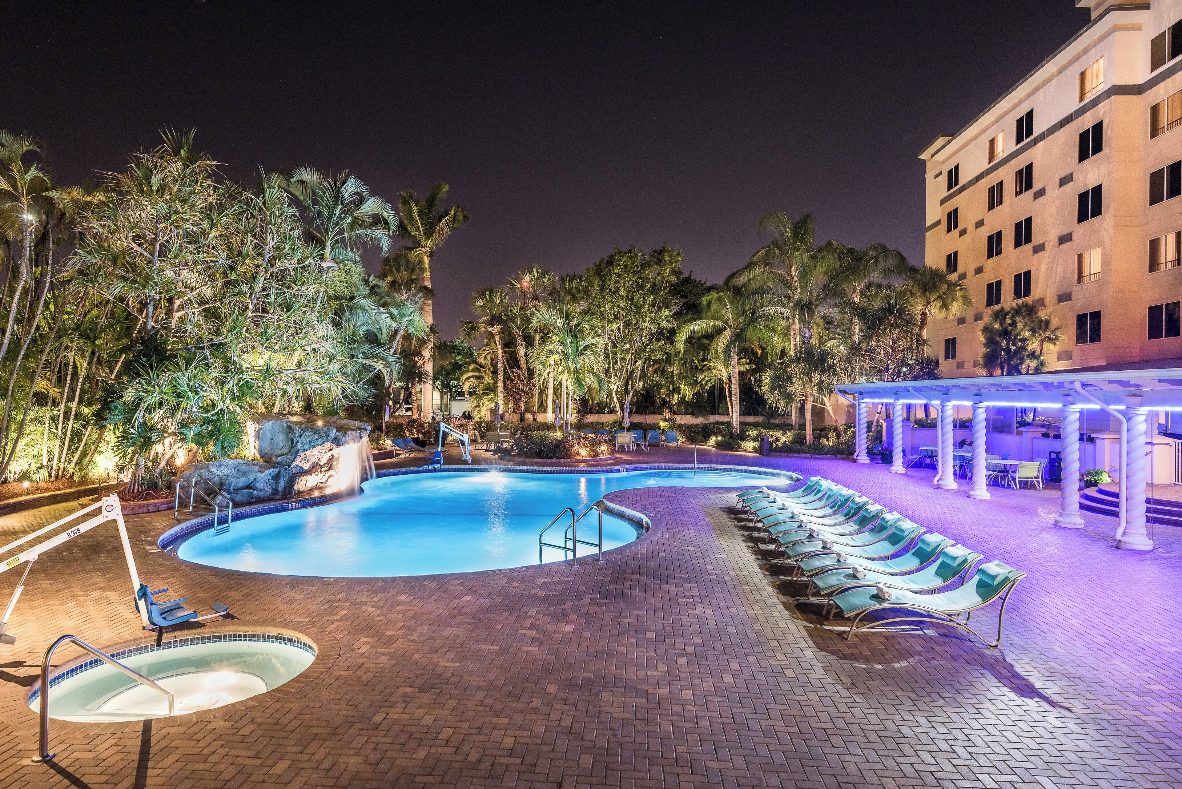 Un área de piscina nocturna con sillas de descanso y un edificio al fondo.