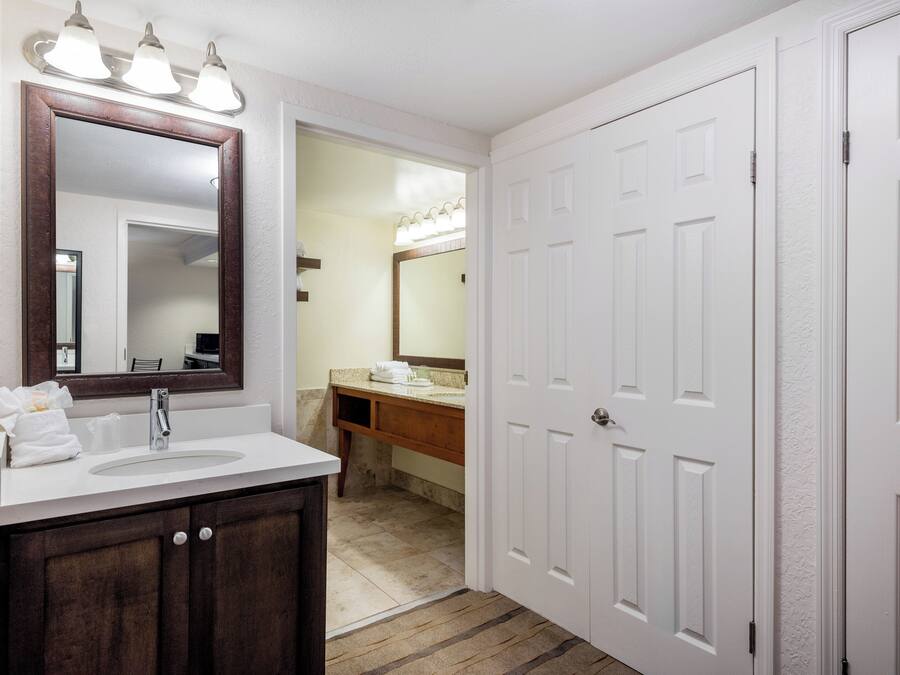 A bathroom with a vanity, a large mirror, a sink, and a door.
