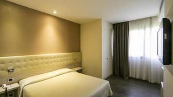 A hotel room with a large bed, a bedside table, a flat-screen TV mounted on the wall, and a window with curtains.