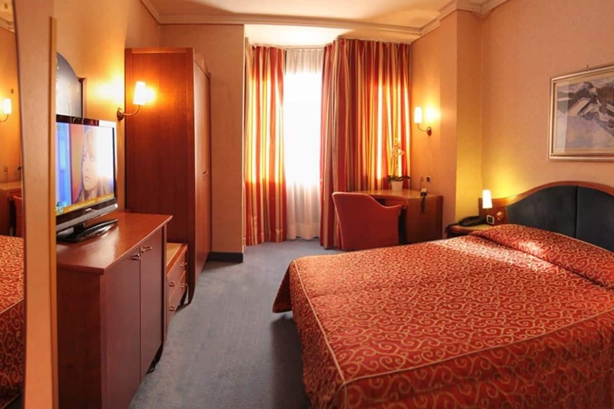 Una camera d'albergo con due letti, una scrivania, una televisione e un bagno.