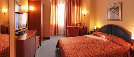 A hotel room with two beds, a desk, a TV, and a bathroom.
