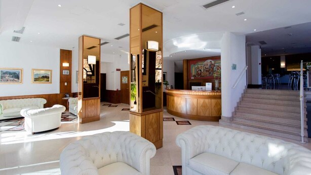A hotel lobby with a reception desk, a staircase, and seating areas.