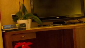 A television on a wooden stand, a potted plant, and a table with a red cup and a white teapot.