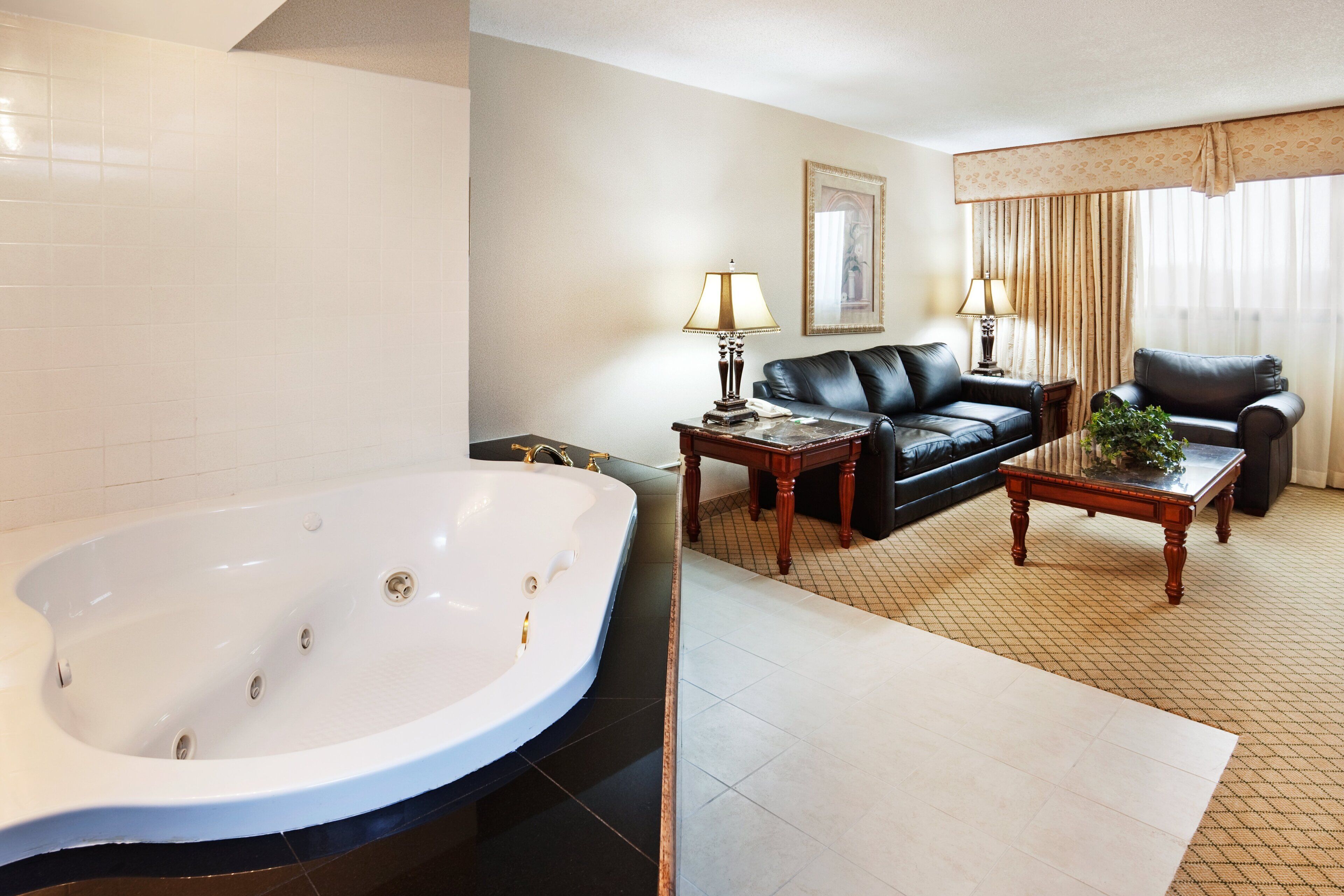 A hotel room with a large bathtub, a black leather sofa, a wooden coffee table, and a framed picture on the wall.