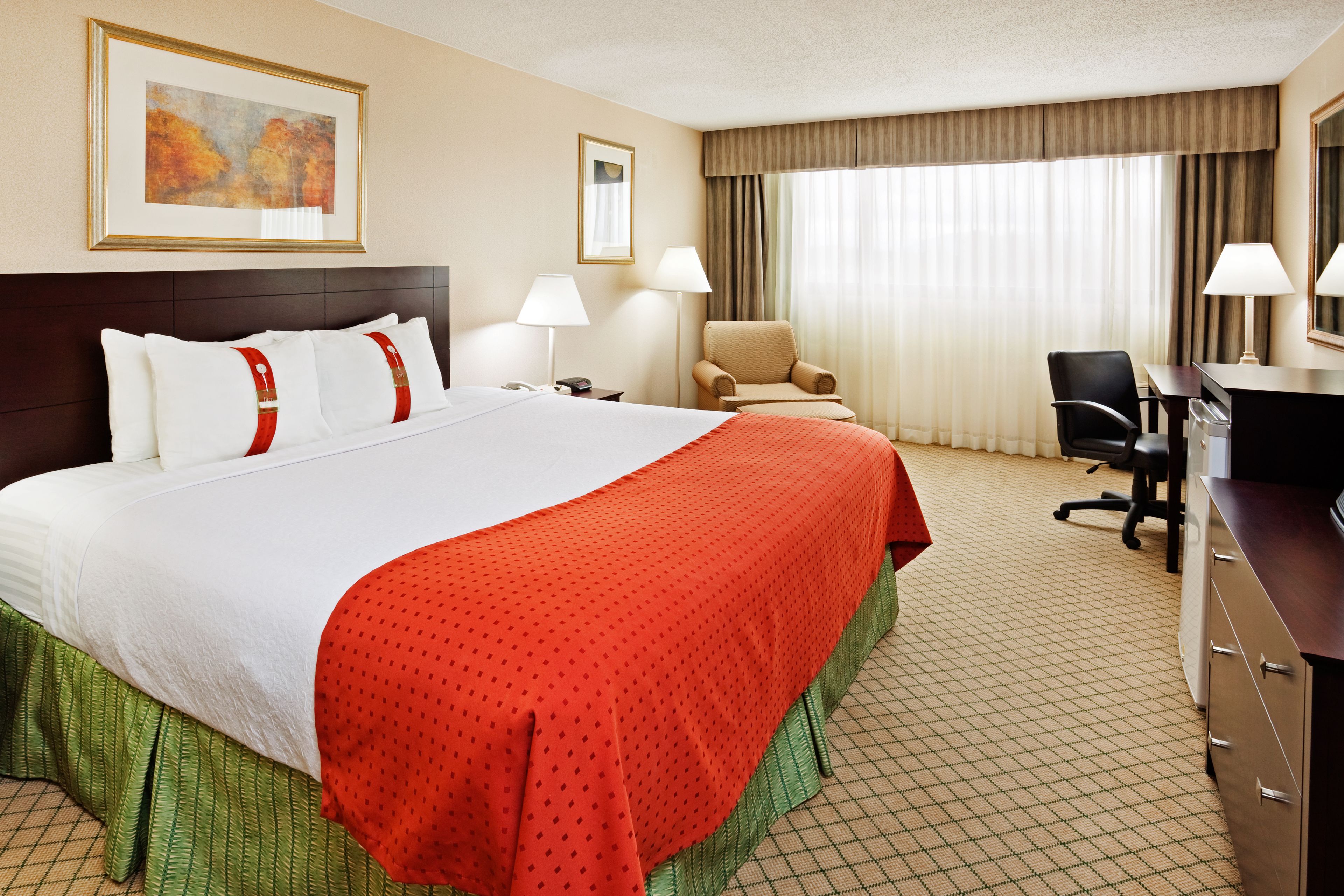 A hotel room with a large bed, two bedside lamps, a desk with a chair, and a window with curtains.