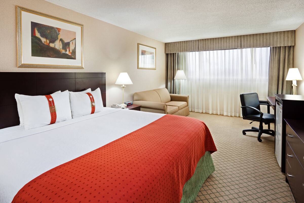 A hotel room with a large bed, a desk, a chair, a sofa, and two lamps.
